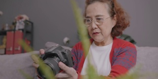 特写镜头和手持:迷人的亚洲高级女性学习在线摄影课程通过笔记本电脑。坐在家里客厅的沙发上和她的老师学习如何用视频通话技术使用数码相机。