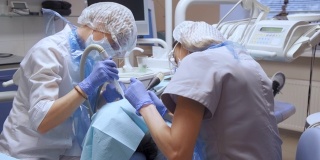两名年轻的女牙医正在一家医院的牙科诊所里做面部保护手术。戴口罩和手套。保健和医学的概念。