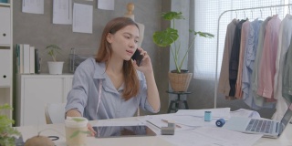 年轻的亚洲女企业家使用智能手机，在家办公与客户交谈。