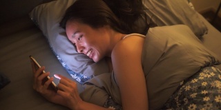 一名亚洲女性在床上使用智能手机