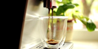 一段把咖啡从咖啡机倒进透明玻璃杯的视频。自制的热美式咖啡。新鲜的咖啡。早晨的咖啡概念与现磨的烘豆。