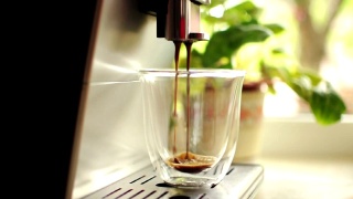一段把咖啡从咖啡机倒进透明玻璃杯的视频。自制的热美式咖啡。新鲜的咖啡。早晨的咖啡概念与现磨的烘豆。视频素材模板下载