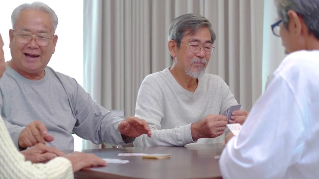 一群60-70岁的亚洲活跃老人与一群快乐的老朋友打牌聊天一起在养老院度过美好的时光。社会的老年人