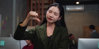 不高兴的亚洲女商人看着相机和做拇指向下的手势在创意办公室。