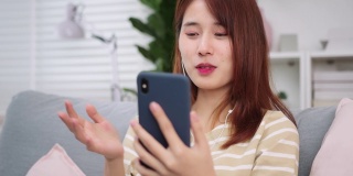 美丽的年轻亚洲女人做一个视频电话微笑和她的朋友和家人在家里交谈。