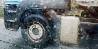 在大雨滂沱的公路上驶过的卡车。车轮在车窗水滴上的细节