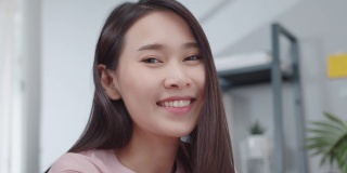 在现代家庭办公室里，美丽的亚洲女商人穿着休闲服装，面带微笑地看着镜头，享受着一个成功的商业项目。