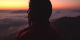 年轻女子看着山上的风景与阳光和雾。带着相机独自旅行的背包客。假日旅游和度假概念。