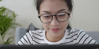 特写亚洲女人的脸戴上眼镜，用笔记本电脑和快乐的微笑，在线学习在家的概念