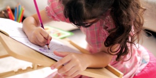 小女孩穿着粉红色的衣服，在家里的客厅里在画册上画画和写字