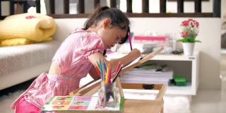 小女孩穿着粉红色的衣服，在家里的客厅里在画册上画画和写字