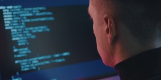 软件开发人员在项目上工作的后视图。一个黑客在霓虹灯下在电脑上工作的肖像。