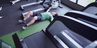 超重的书呆子在跑步机上跑累了，倒在健身房的地板上
