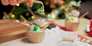 在厨房里用镊子夹上奶油和糖糖霜银球装饰帽子，这是为冬天传统节日圣诞节准备烘焙糕点和甜点的特写镜头。