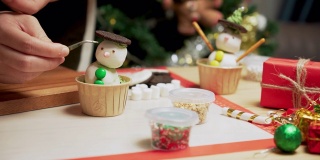 在装饰着圣诞树和装饰品的厨房里，准备冬天传统节日圣诞节的烘焙食品和甜点架，用糖霜自制纸杯蛋糕做一个雪人，用镊子给眼睛加巧克力