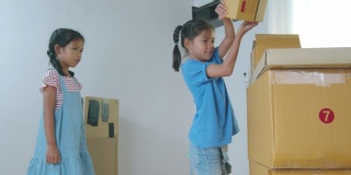 在搬家日，两个亚洲女孩帮助父母在搬家前准备盒子里的东西。家居装修和搬迁概念。慢动作镜头。