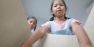 两个亚洲女孩帮助父母把东西放进盒子和关闭盒子搬迁前的日子。家居装修和搬迁概念。慢动作镜头。