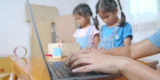 女人在笔记本电脑上打字，接收和检查网上购物订单。孩子正在把地址写进盒子里，帮助家长为在线客户准备送货盒。