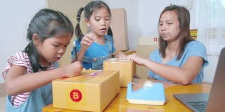 两个小女孩帮助家长在盒子里写上地址，用胶带把产品包装好，然后邮寄给在线客户，充满乐趣和快乐。