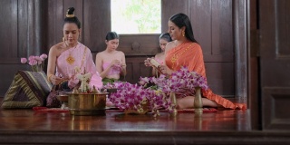 一群从事花环制作的泰国妇女，她们还穿着泰国传统服装，住在古老的房子里