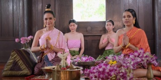 一群穿着泰国传统服装带着鲜花的泰国妇女呆在古老的房子里，向照相机表示敬意