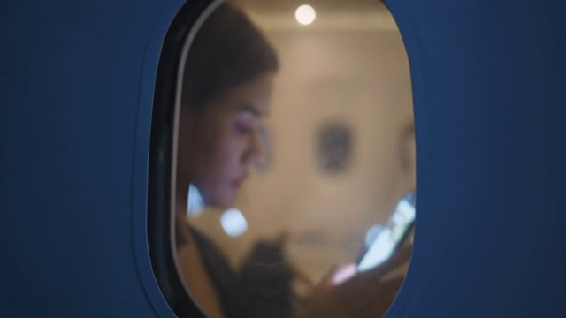 亚洲女性乘客在飞机上使用智能手机，从飞机窗外看