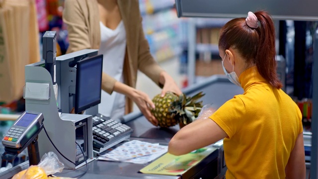 收银员戴着防护口罩和手套用扫描仪刺穿产品。在隔离期间在超市购物。4 k, ProRes