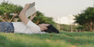 迷人的美丽年轻的亚洲女性轻松地阅读，而躺在地板上的草。