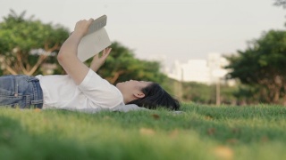 迷人的美丽年轻的亚洲女性轻松地阅读，而躺在地板上的草。视频素材模板下载