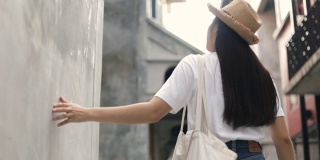 美丽的亚洲女人戴着一顶复古的帽子，拿着一个布袋，用手轻轻地触摸墙壁。