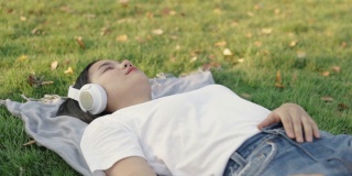 美丽的亚洲女性戴着耳机听音乐，睡在家里的草地上。