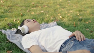 美丽的亚洲女性戴着耳机听音乐，睡在家里的草地上。视频素材模板下载
