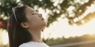年轻的亚洲女人的近距离肖像放松享受和平的日落，抬头呼气新鲜空气放松在一个美丽的夏季日落公园。