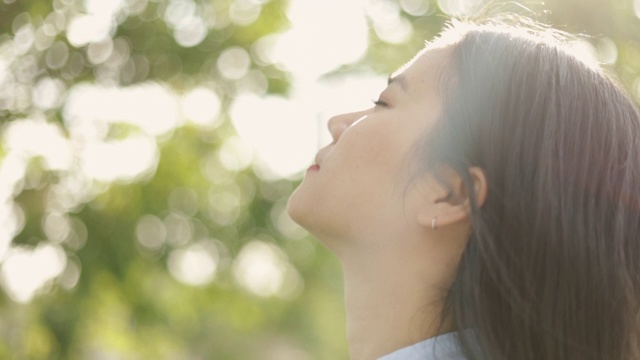 年轻的亚洲女人的近距离肖像放松享受和平的日落，抬头呼气新鲜空气放松在一个美丽的夏季日落公园。