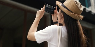年轻美丽的亚洲旅行者戴着复古的帽子，用智能手机拍摄建筑照片。