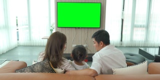 亚洲幸福家庭坐在家里的客厅看电视，一起度过有质量的时间活动在假期，假日，幸福或生活方式的概念。