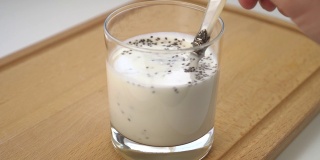 将粘稠的酸乳或酸奶与奇亚籽混合在玻璃杯中，放在木砧板上。