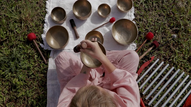 身穿粉色和服的金发女子在沉思的喜马拉雅歌唱碗上弹奏。