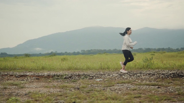 美丽的亚洲女人在乡村公路上跑步，山景美丽的早晨。