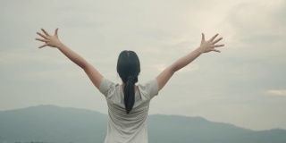 年轻的亚洲女子在运动服装高举在空中的山景感觉幸福。