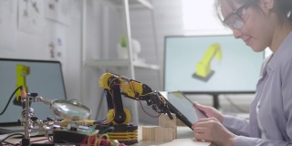 女工程师正在他的车间里研究创新技术机械机器人手臂，她用数字平板电脑用手控制机器人手臂