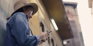 在泰国的一条小街上，一名亚洲女性用智能手机打字滚动新消息的社交媒体。