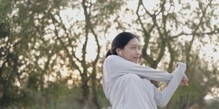 美丽的亚洲女人跑步运动员听音乐穿着运动服伸展双臂举起感觉放松慢跑健康的生活方式锻炼在海边在日出。