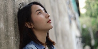 美丽年轻的亚洲女性孤独的感觉倚在墙上在泰国曼谷的一个小街道。