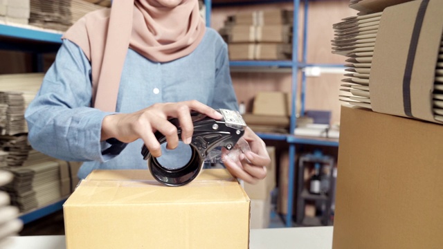 4K超高清接近多莉缩小:伊斯兰穆斯林女性亚洲仓库工人包装包裹在仓库配送中心。应用于商业仓储物流的概念。