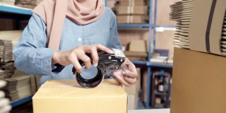 4K超高清接近多莉缩小:伊斯兰穆斯林女性亚洲仓库工人包装包裹在仓库配送中心。应用于商业仓储物流的概念。