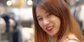 一个美丽快乐的年轻亚洲少女的肖像女人看着相机和一个愉快和快乐的表情站在一个购物商店，享受她的假期或周末。