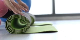瑜伽室活跃的生活方式年轻的亚洲妇女在房间里滚动运动垫为早上的背景。在工作室里锻炼，冥想瑜伽垫，木地板上的瑜伽球。运动的概念。