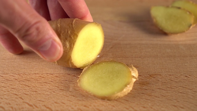 一名男子用刀将多汁的生姜切成块。在一块木板上。
