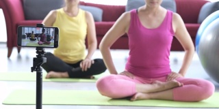 年轻的亚洲夫妇穿着运动服，一边在家做瑜伽，一边在镜头前录制关于健康生活方式的视频博客或短视频。两个可爱的女人在做关于瑜伽和健康生活方式的视频博客。